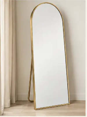 Full-length brass-framed mirror beside cream linen curtains